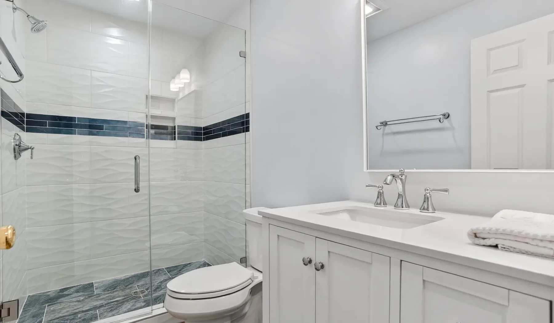 A bathroom with a glass shower and a white vanity.