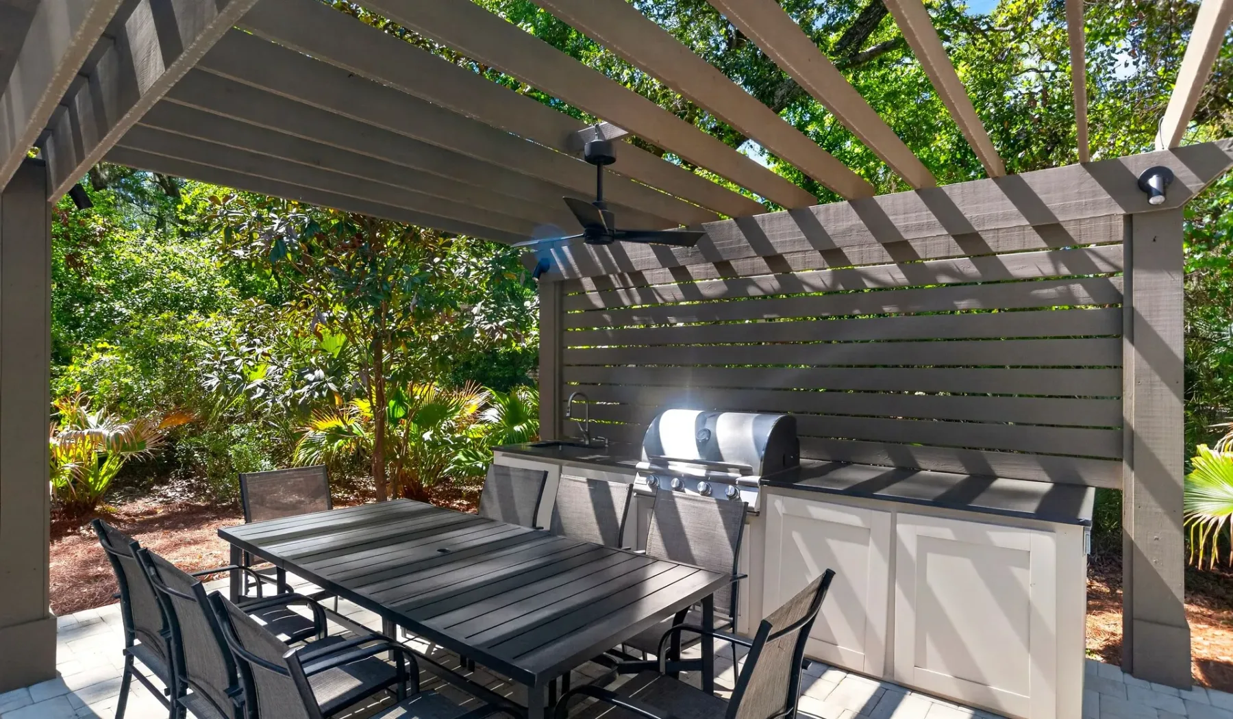 A shaded outdoor dining area with a table, seating, and a built-in grill.