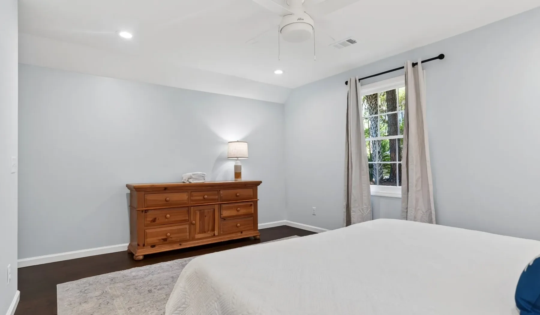 A bedroom with a bed, wooden dresser, and window with curtains.