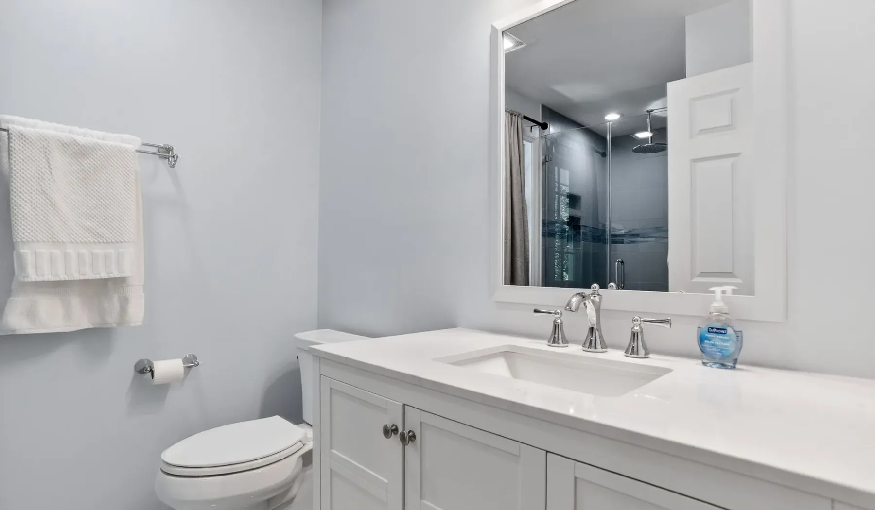 A bright bathroom with a white vanity, mirror, and glass shower.