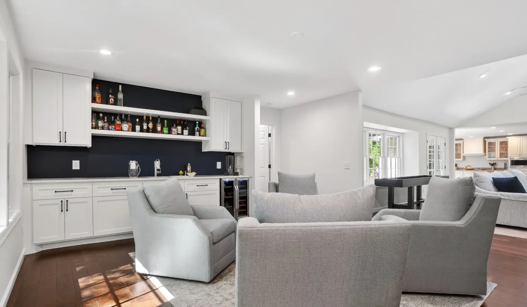 An open-plan living room with gray seating beside a kitchen and dining area.