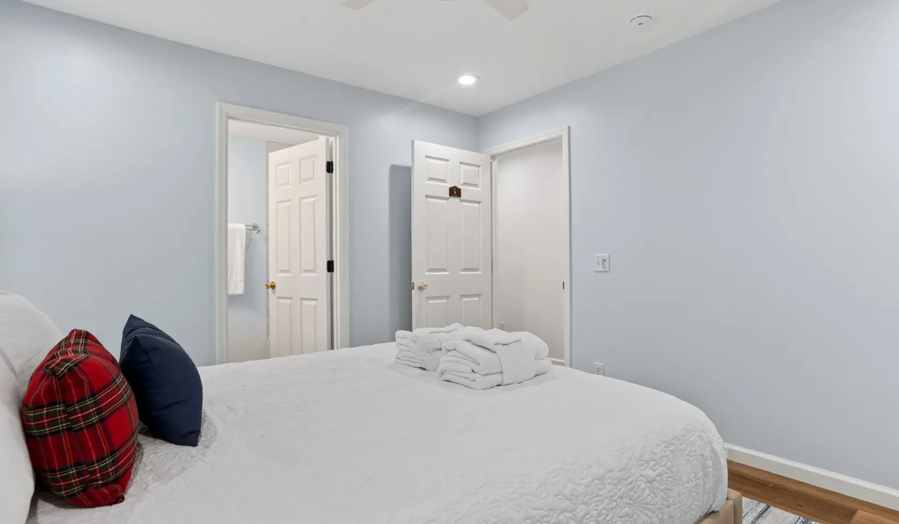 A bedroom with a bed and folded towels, with open doors in the background.