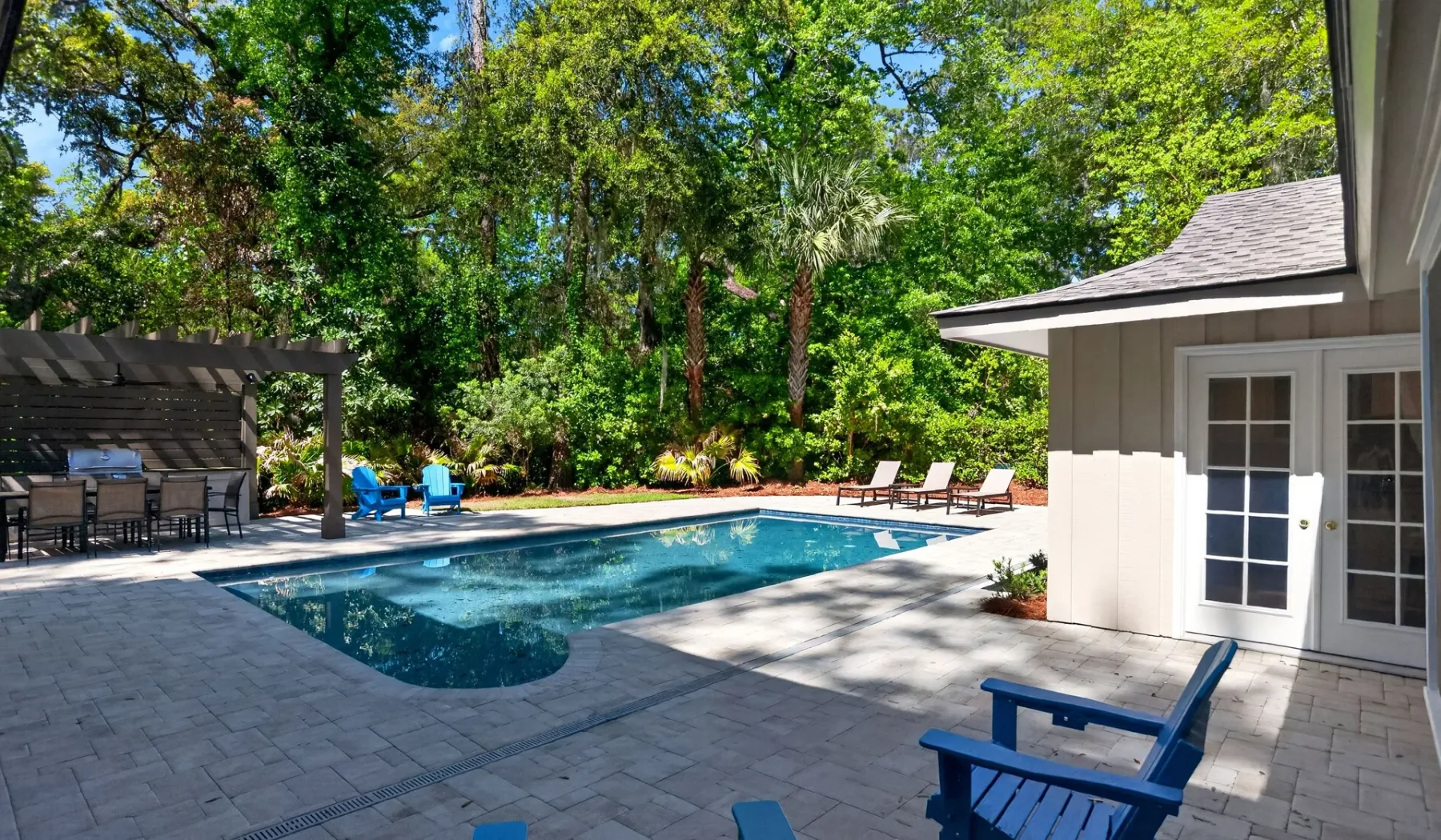 A swimming pool sits beside a paved patio, shaded by surrounding trees.