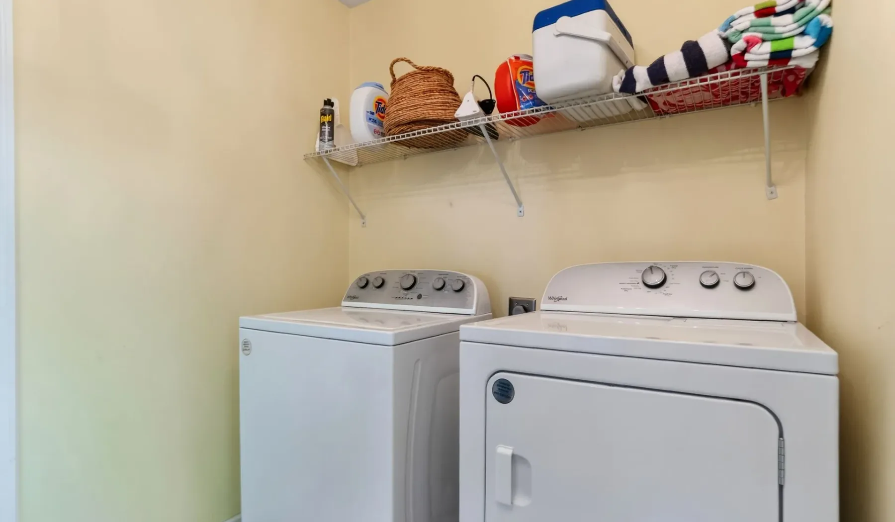 A laundry room with a washer and dryer beneath a wall shelf.