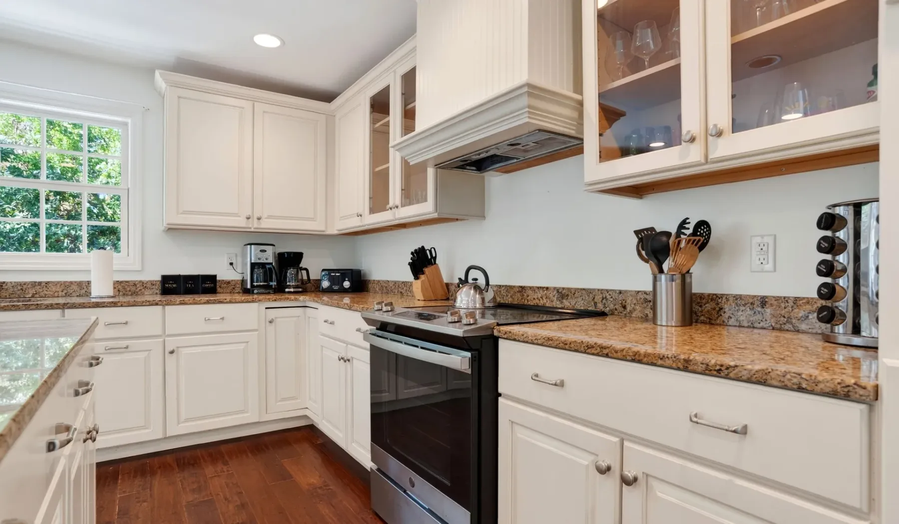 A bright kitchen with white cabinetry, stone countertops, and a central range.