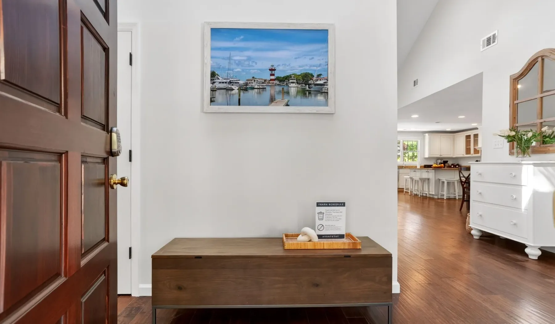 An entryway with a wooden console table and framed waterfront artwork.