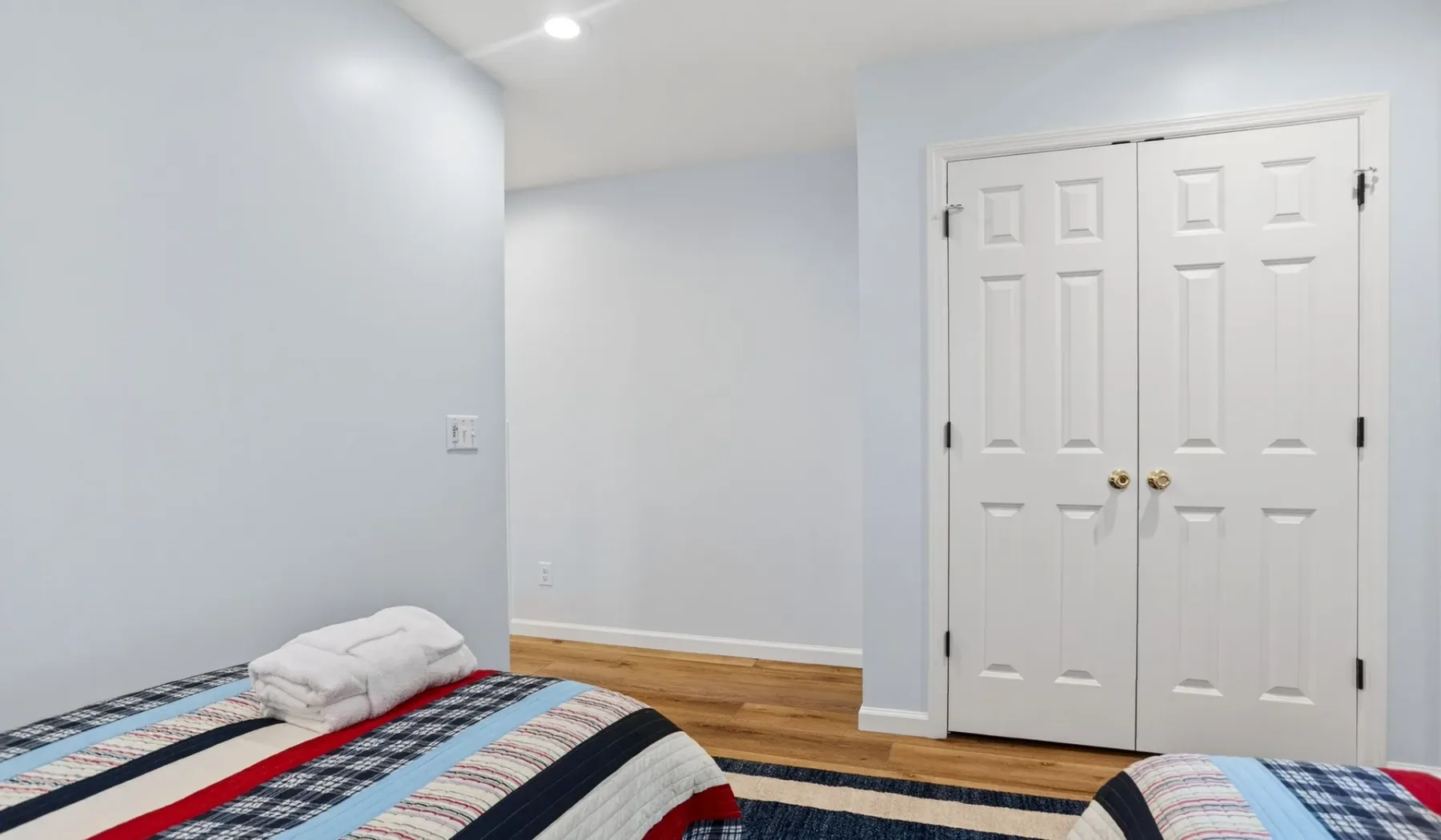A bedroom with a patterned bedspread and white double closet doors.