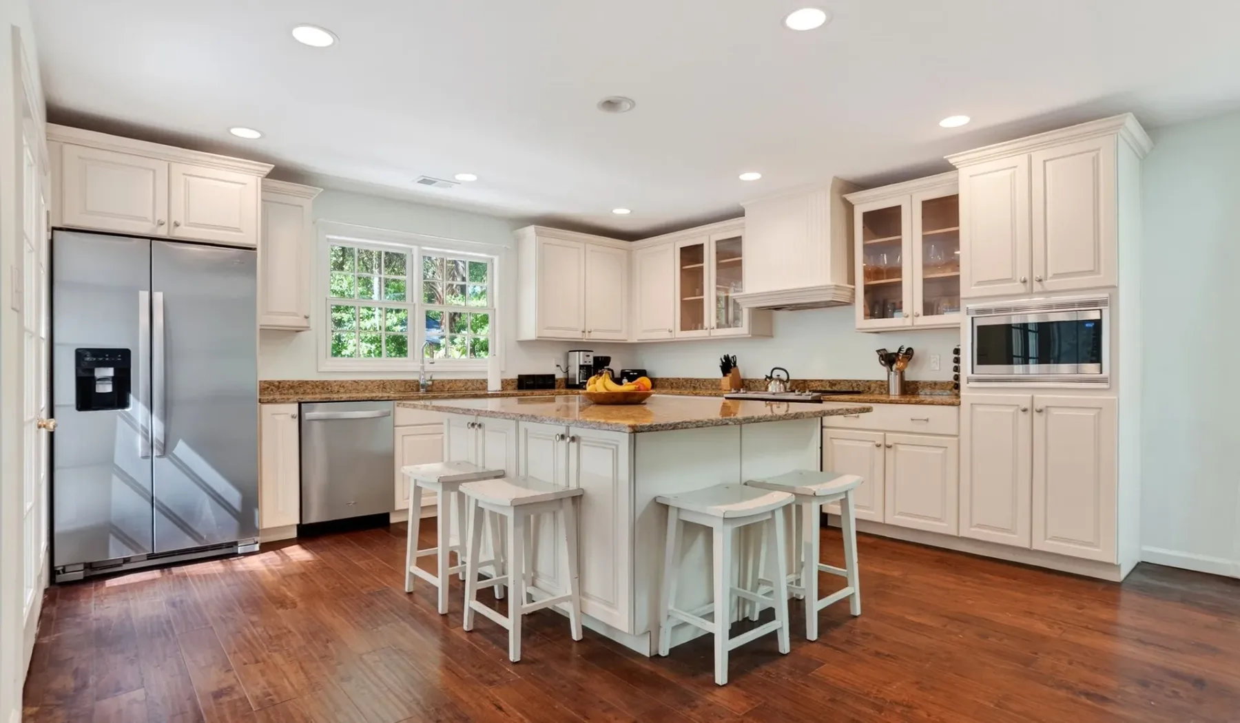 A bright kitchen with a central island, bar seating, and stainless steel appliances.