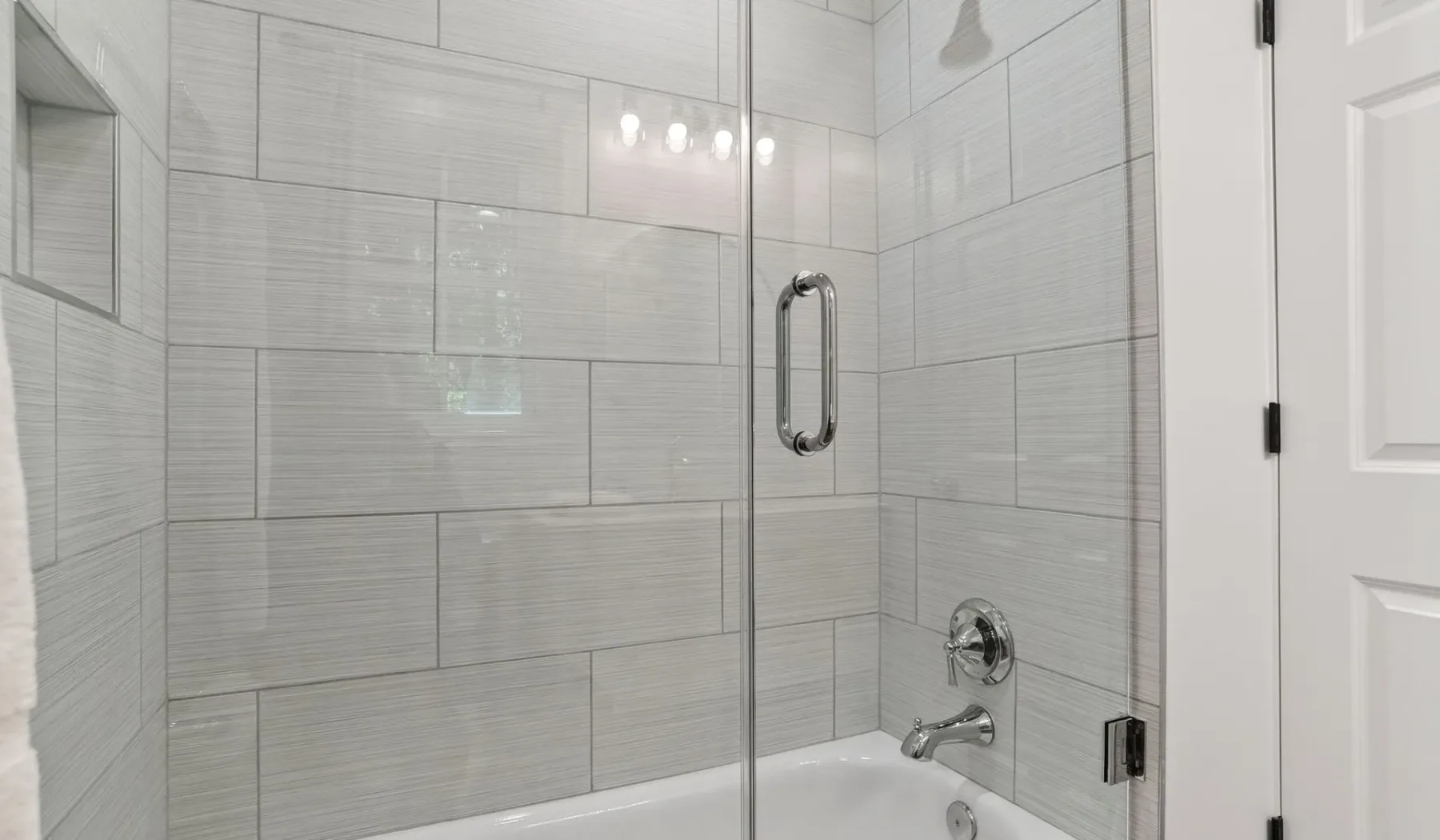 A tiled bathroom shower beside a white bathtub.