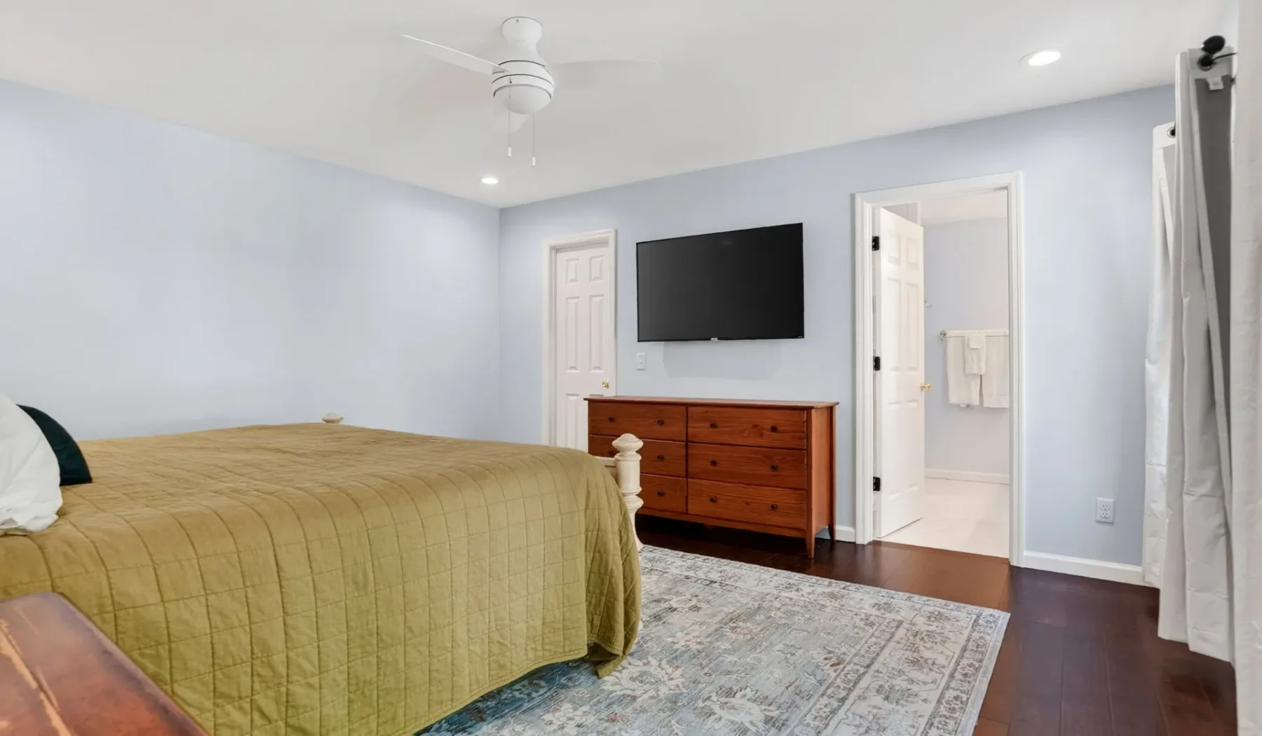 A bedroom with a bed, dresser, and wall-mounted television.