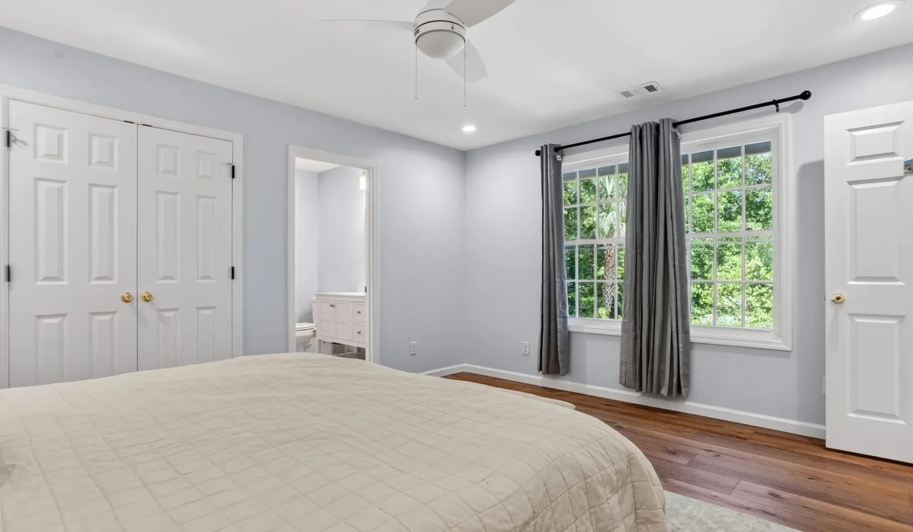 A bedroom with a bed, gray curtains, and windows overlooking greenery.