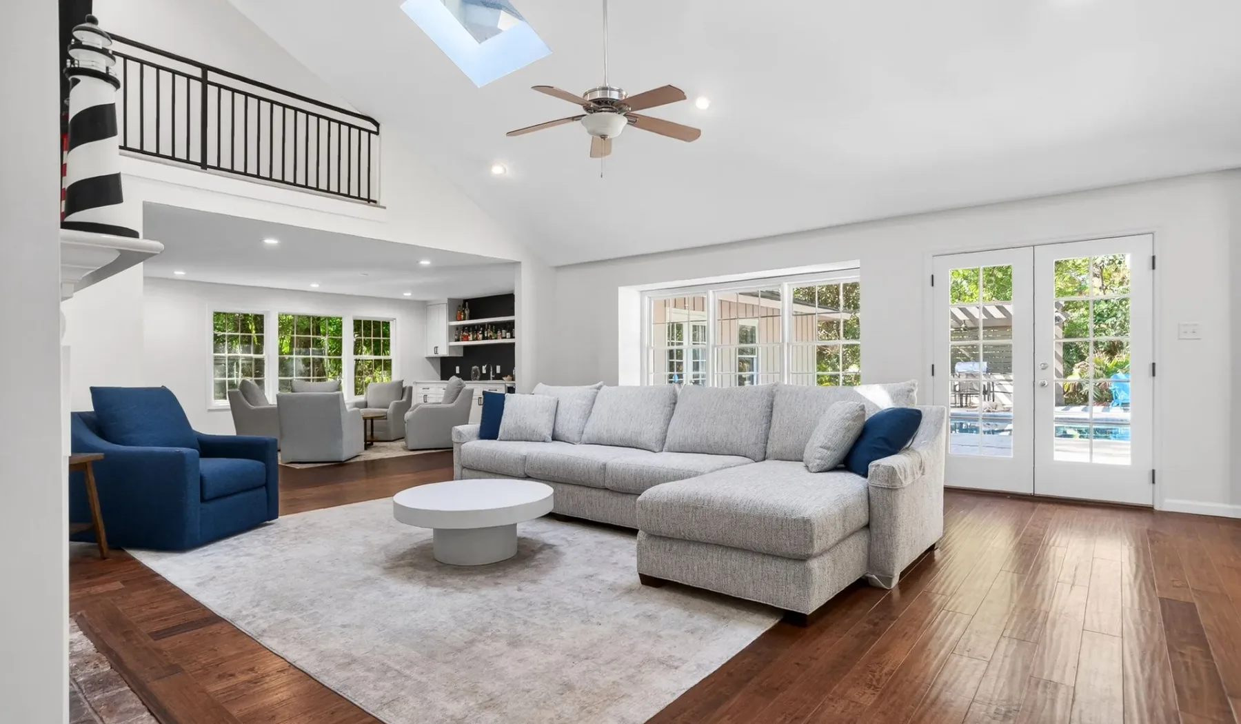 A bright living room has a large gray sectional sofa, blue seating, and glass doors.