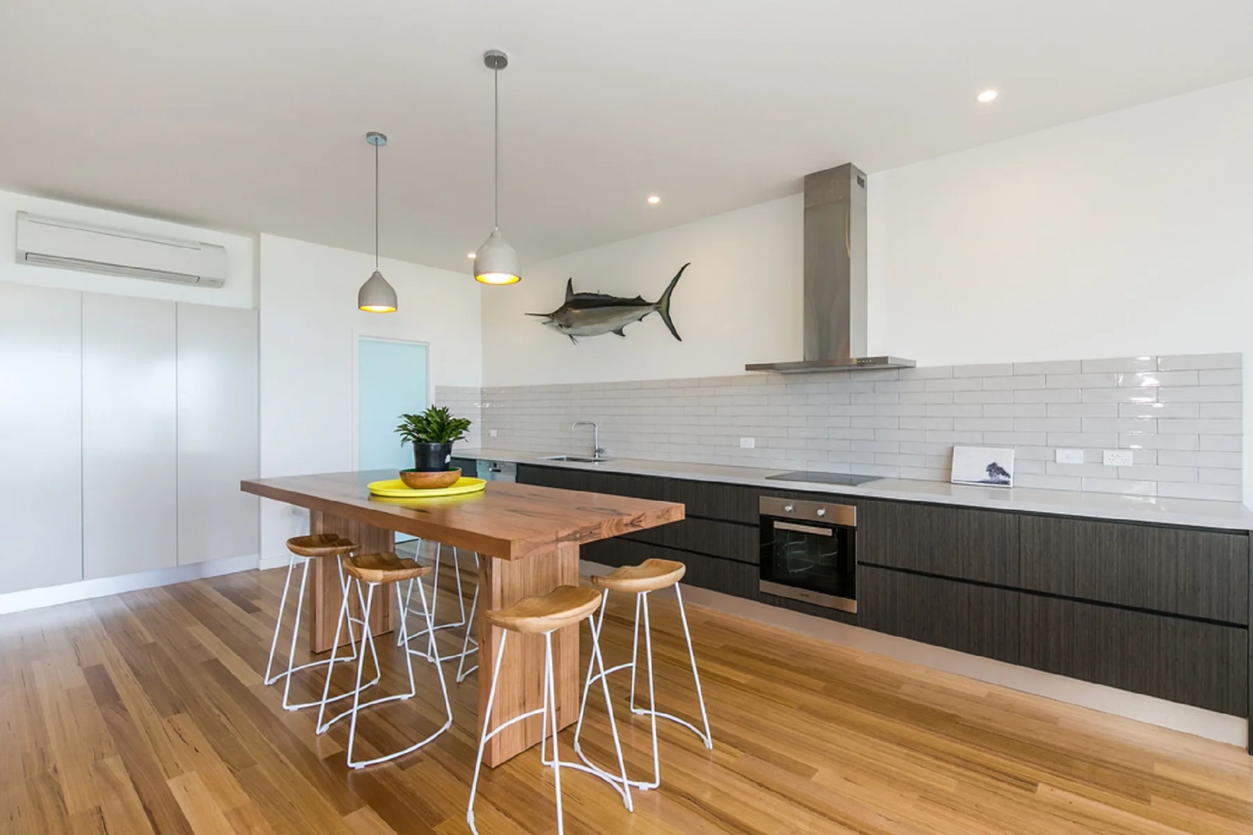 A modern kitchen with a wooden dining table and pendant lights.