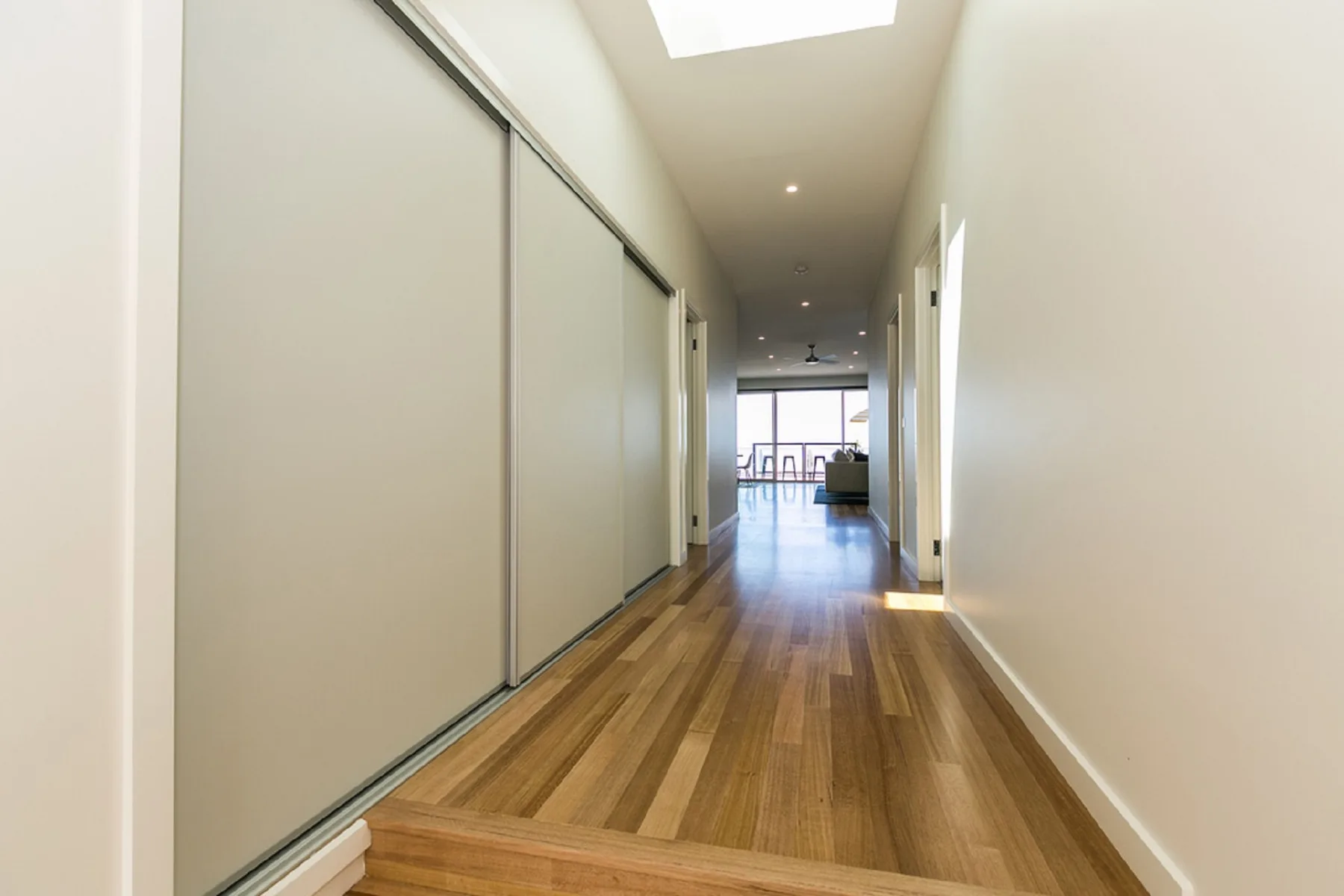 A bright hallway with wooden flooring leads toward a living area.