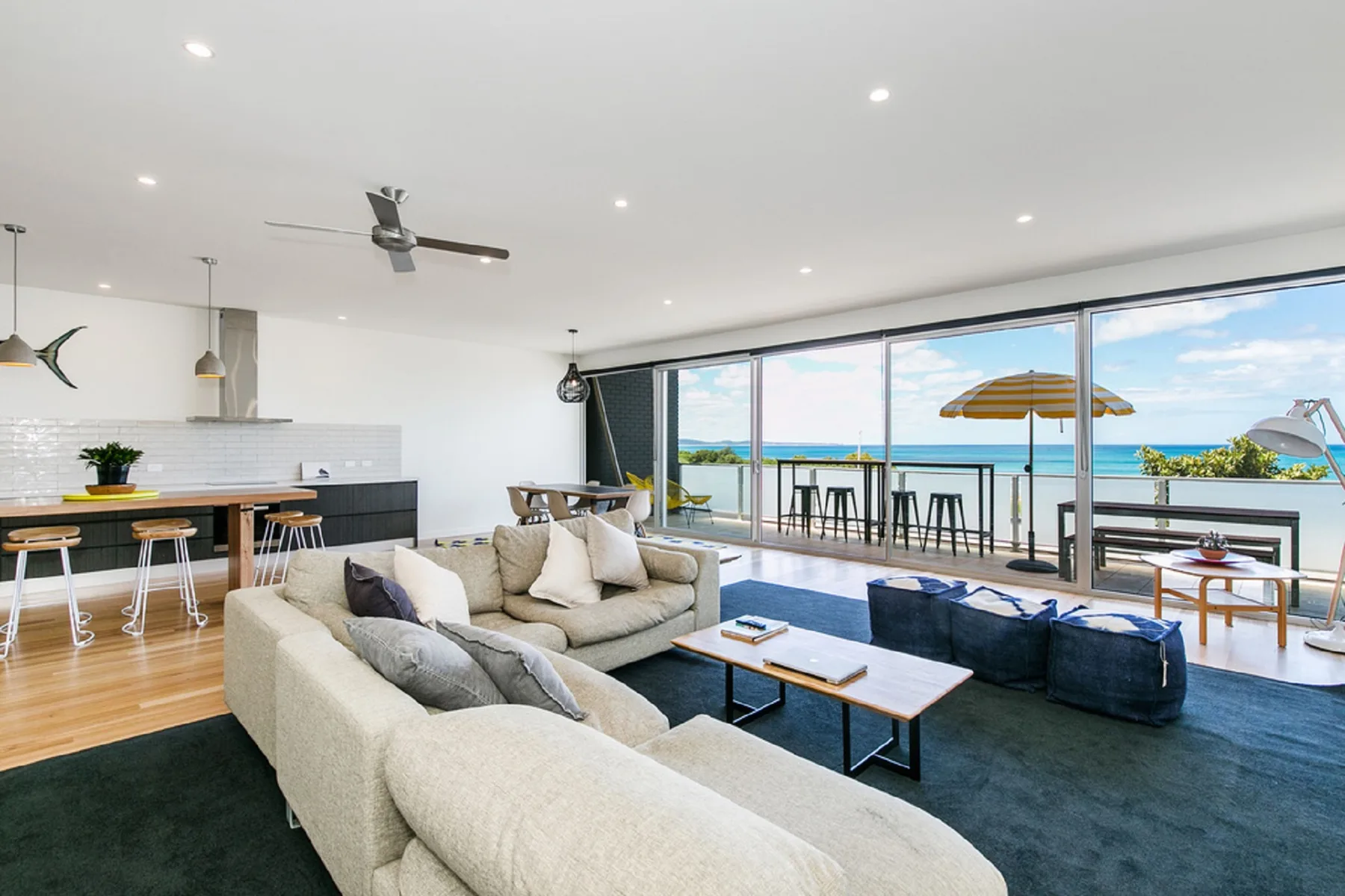 An open-plan living room and kitchen face large windows overlooking the ocean.