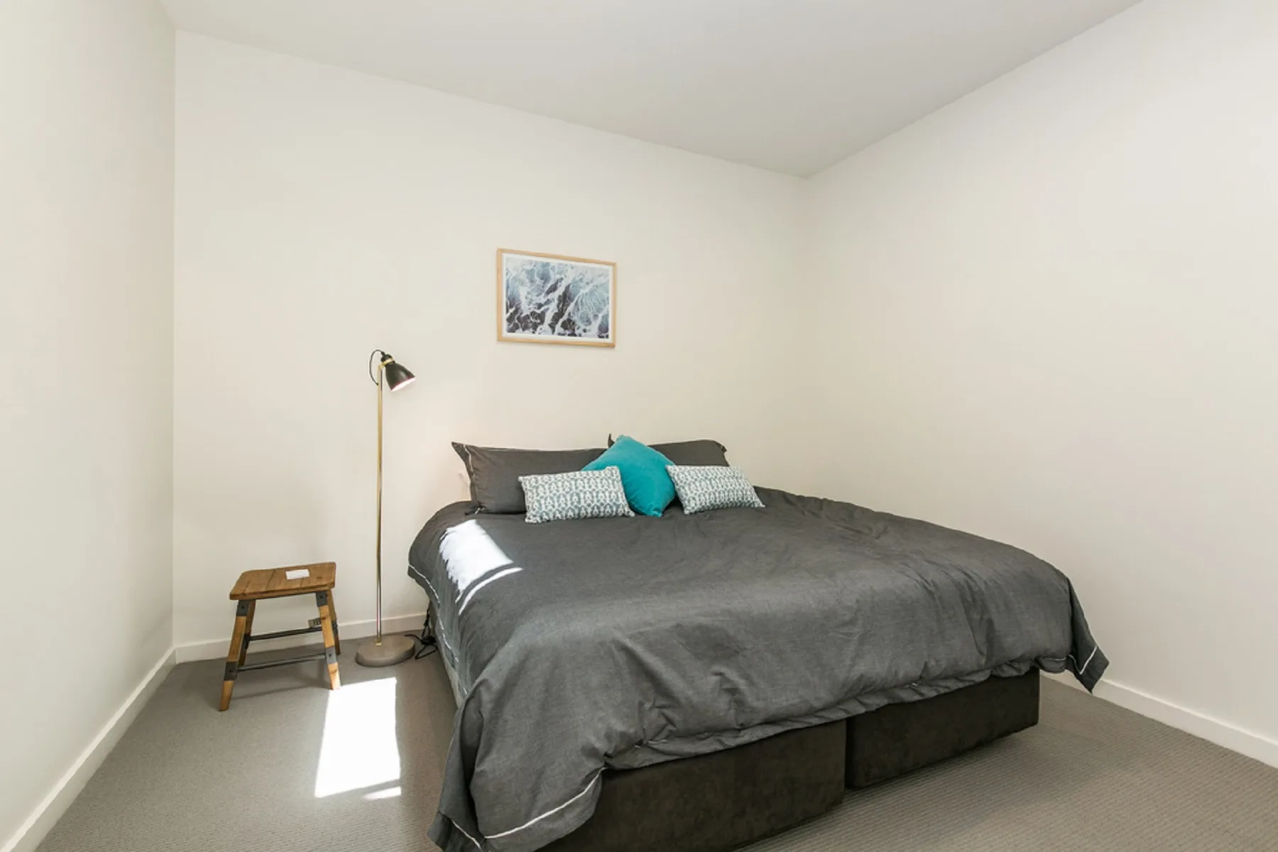 A bedroom with a neatly made bed and a small framed picture on the wall.