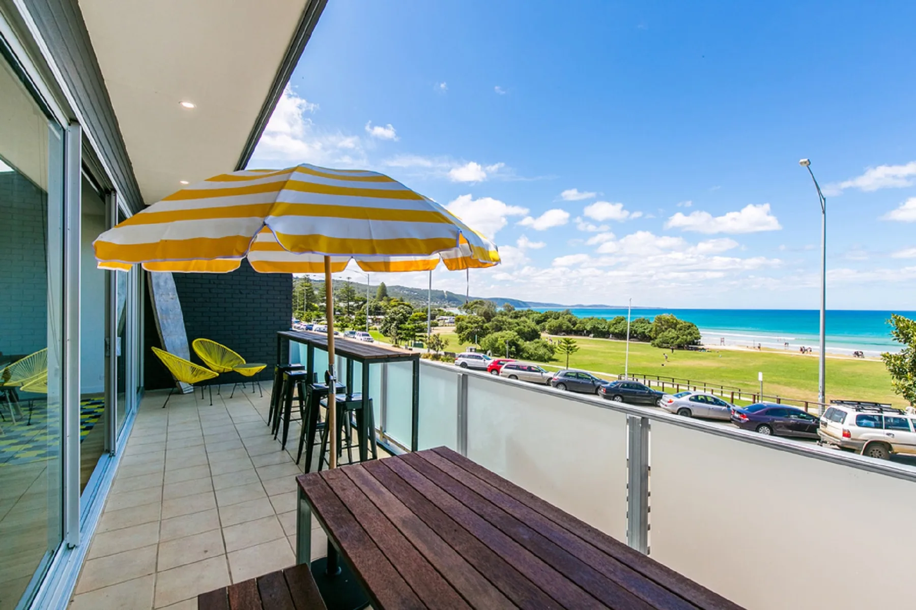 A balcony seating area overlooks a grassy beachfront and the ocean.