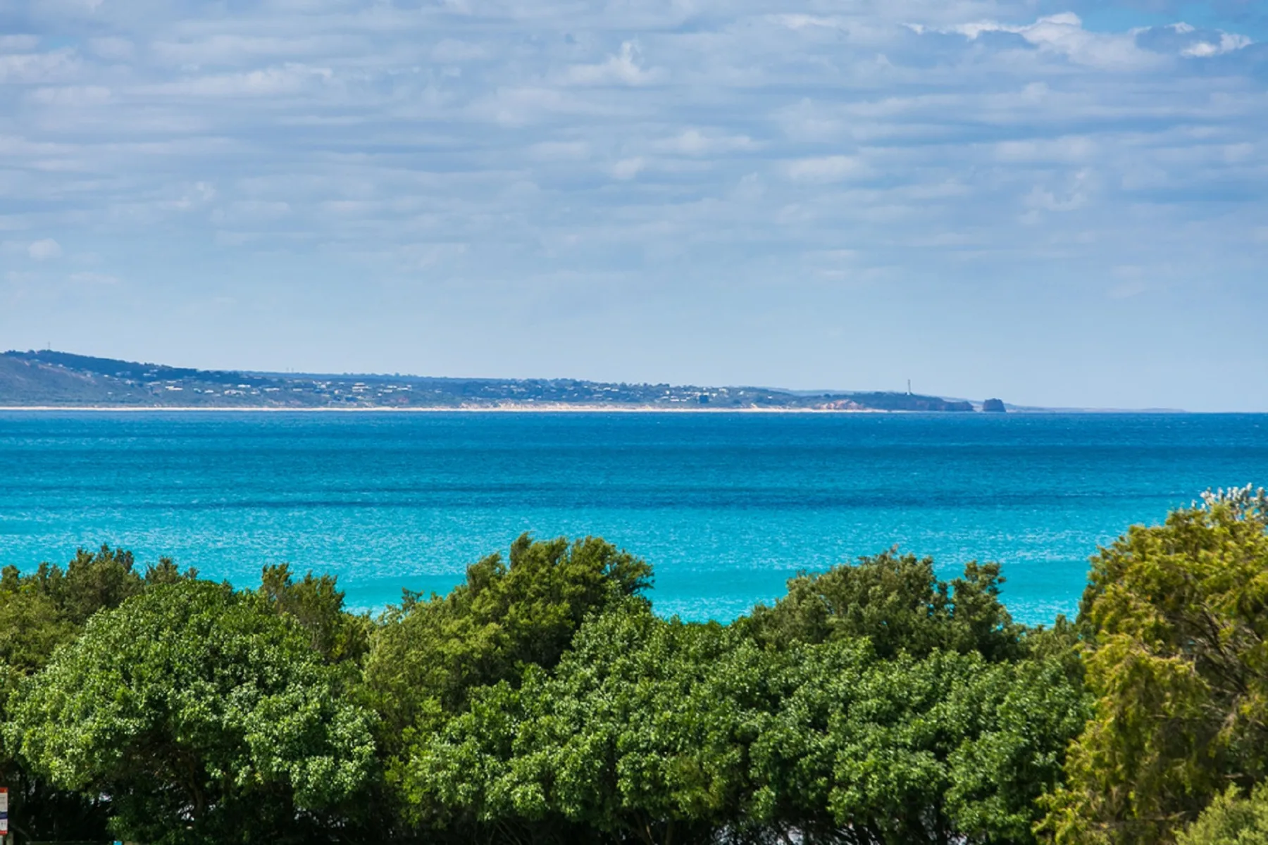 A coastal landscape with turquoise water, distant shoreline, and green trees.
