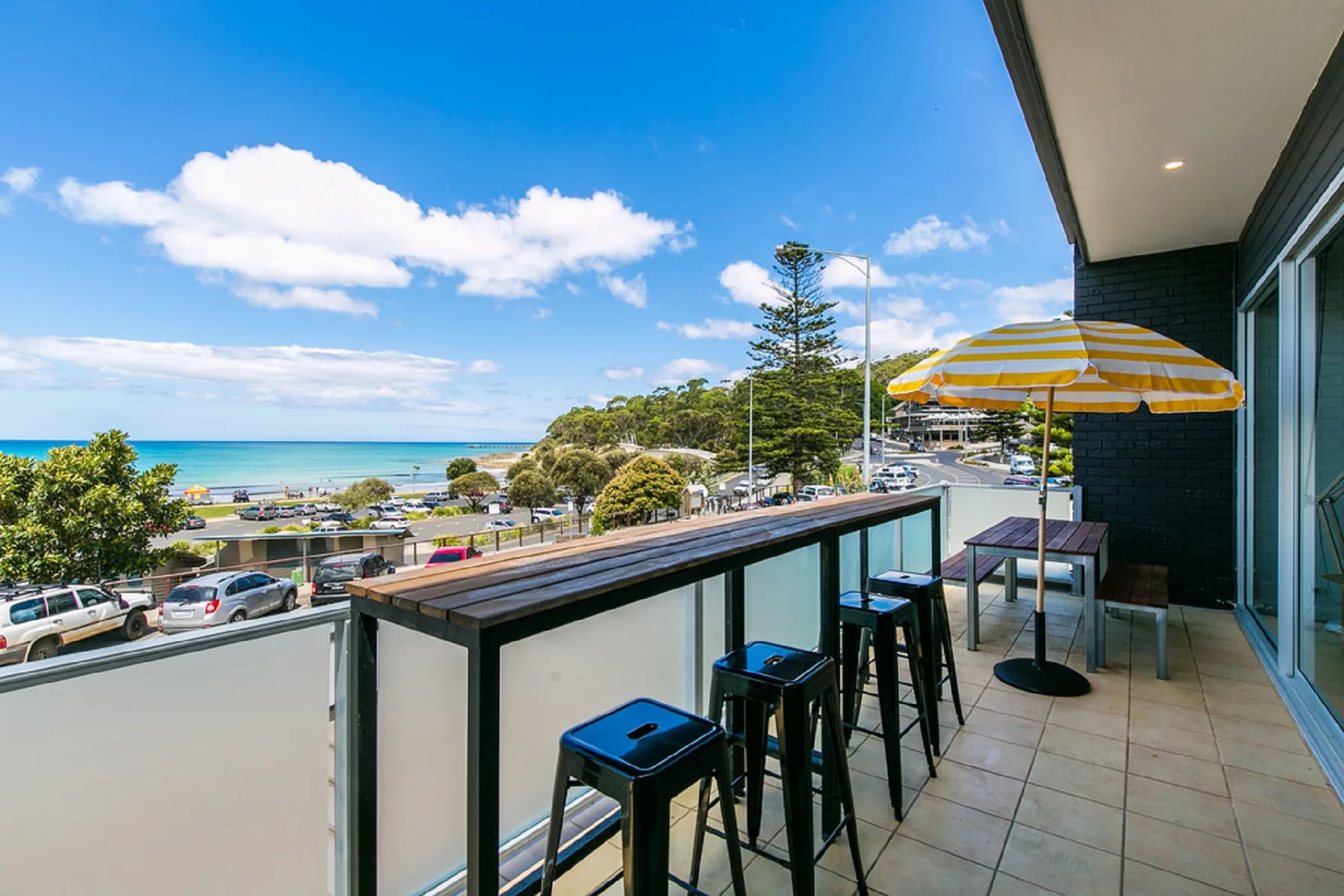 A balcony with seating and a striped umbrella overlooks the ocean.
