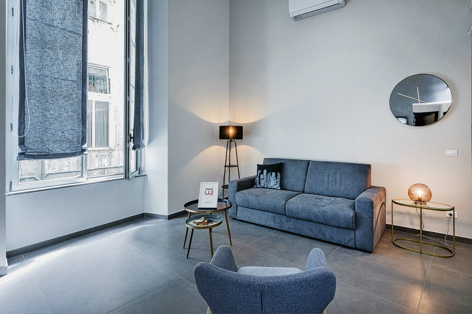 A living room with a blue sofa, small tables, and a large window.