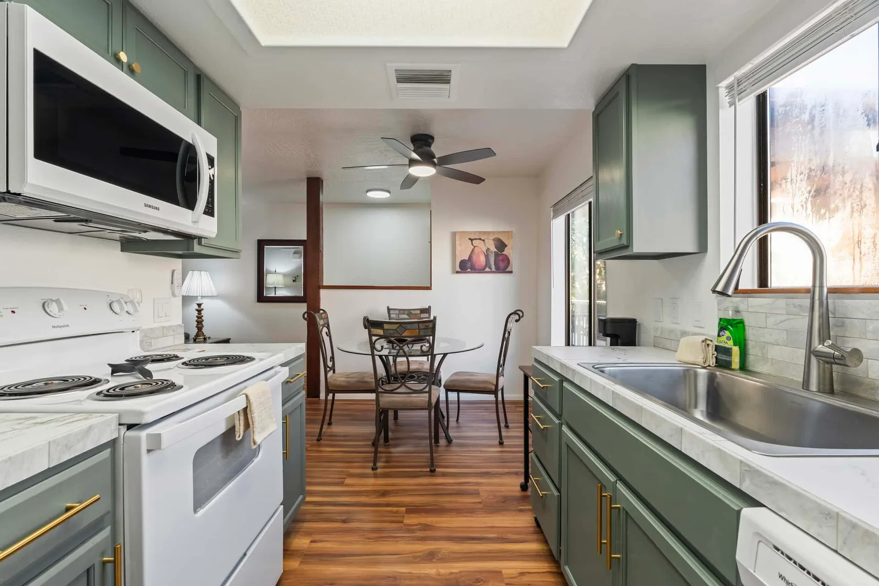 A compact kitchen with green cabinetry, a dining table, and a large window.