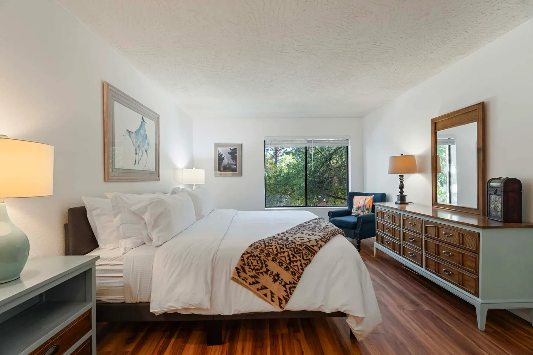 A bright bedroom with a bed, a window, and a wooden dresser.