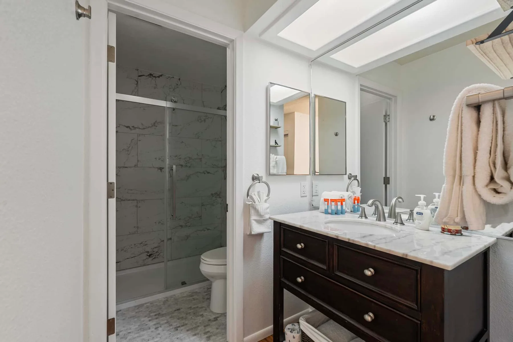 A bathroom vanity with a mirror stands beside a shower.