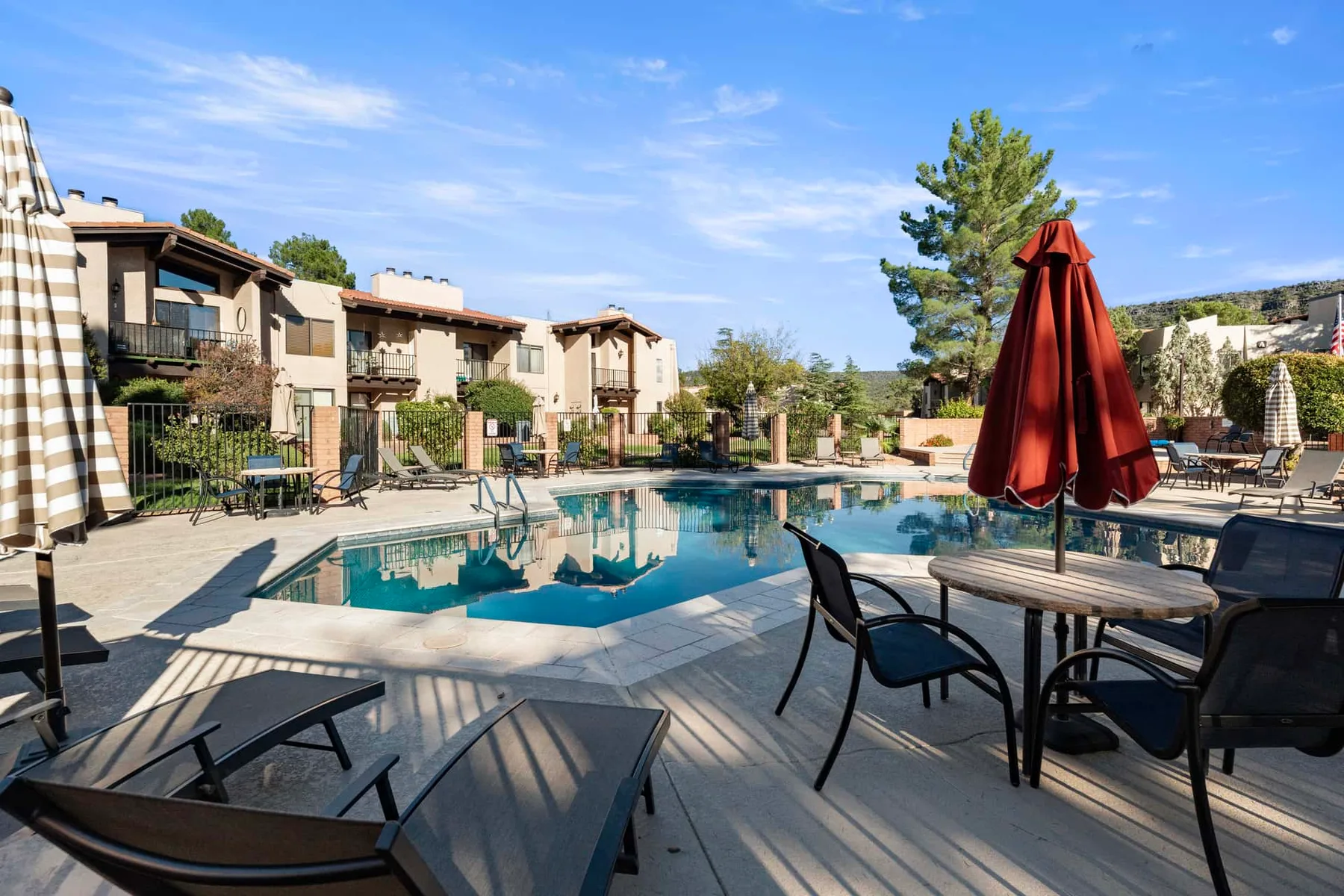 An outdoor swimming pool is surrounded by patio seating and residential buildings.