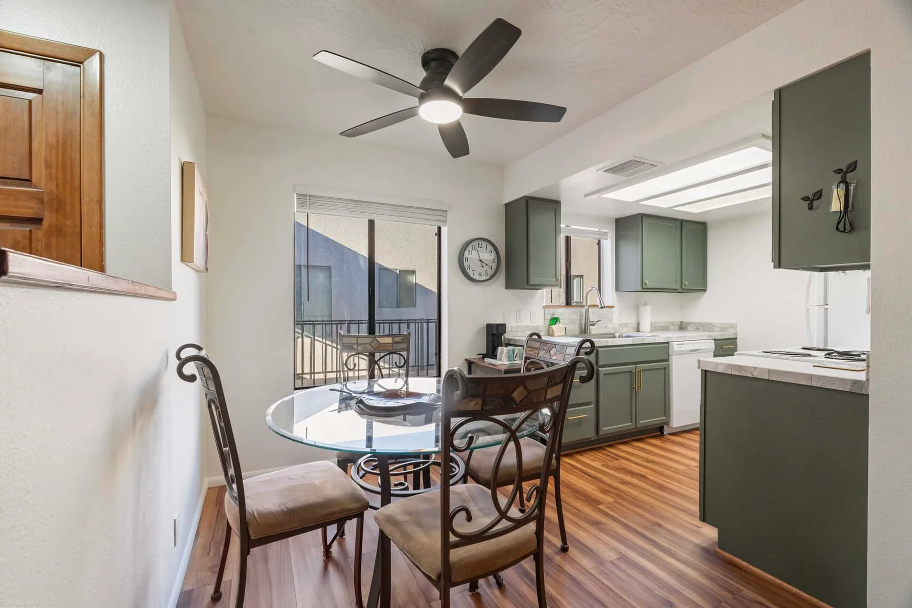 An open dining area and kitchen with a glass table and green cabinets.