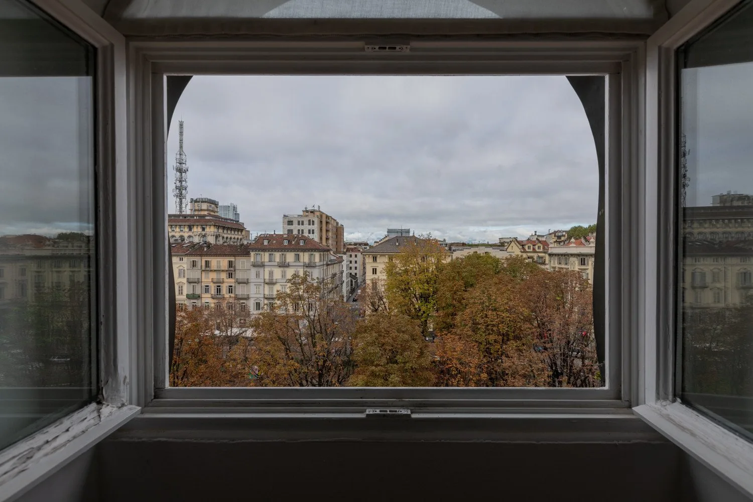 A city view through an open window, with buildings and autumn-colored trees.