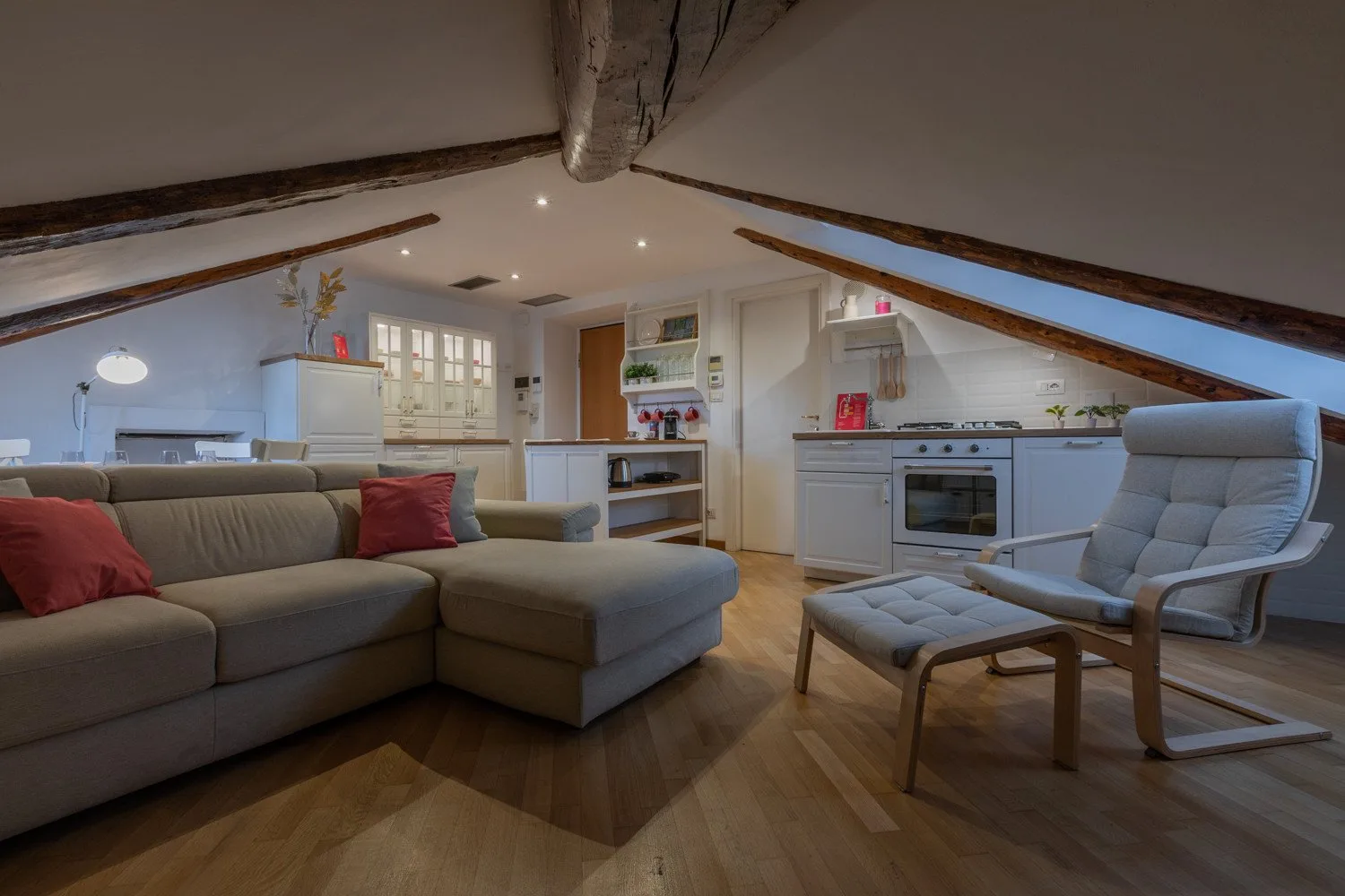 Sala de estar y cocina de planta abierta bajo un techo inclinado, con asientos y una barra.