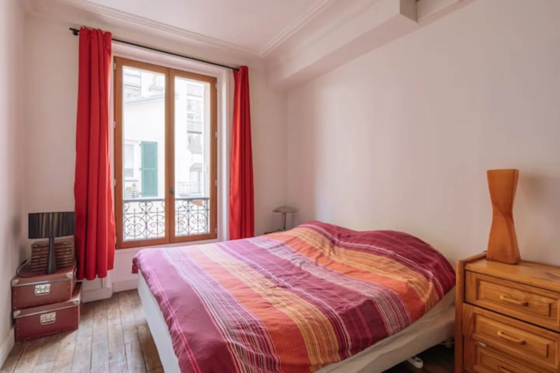 A bedroom with a bed covered in colorful striped bedding beside a window.
