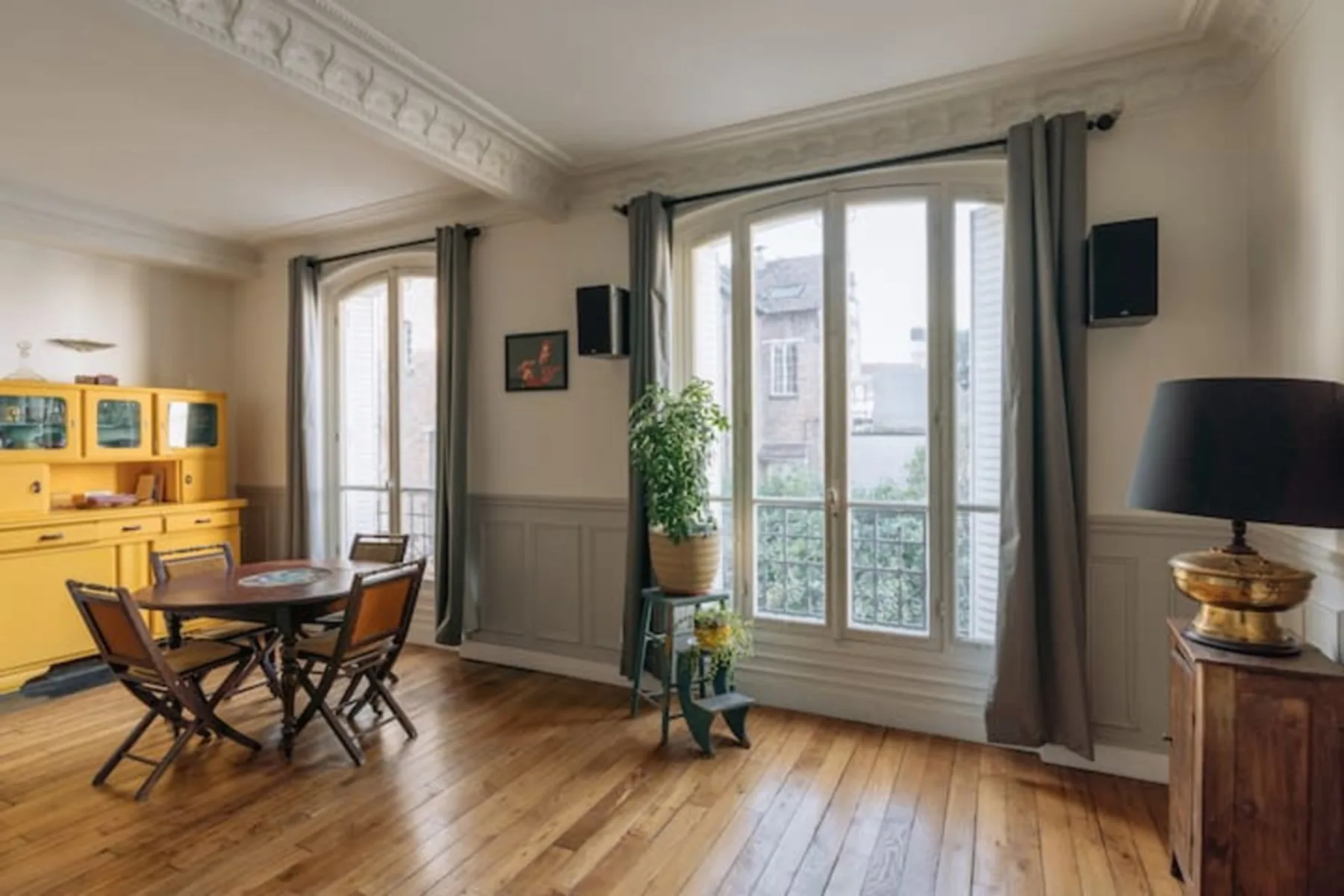 A dining area with a wooden table beside tall windows and a yellow cabinet.