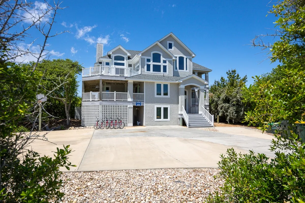 A large coastal-style house stands beside a wide paved driveway.
