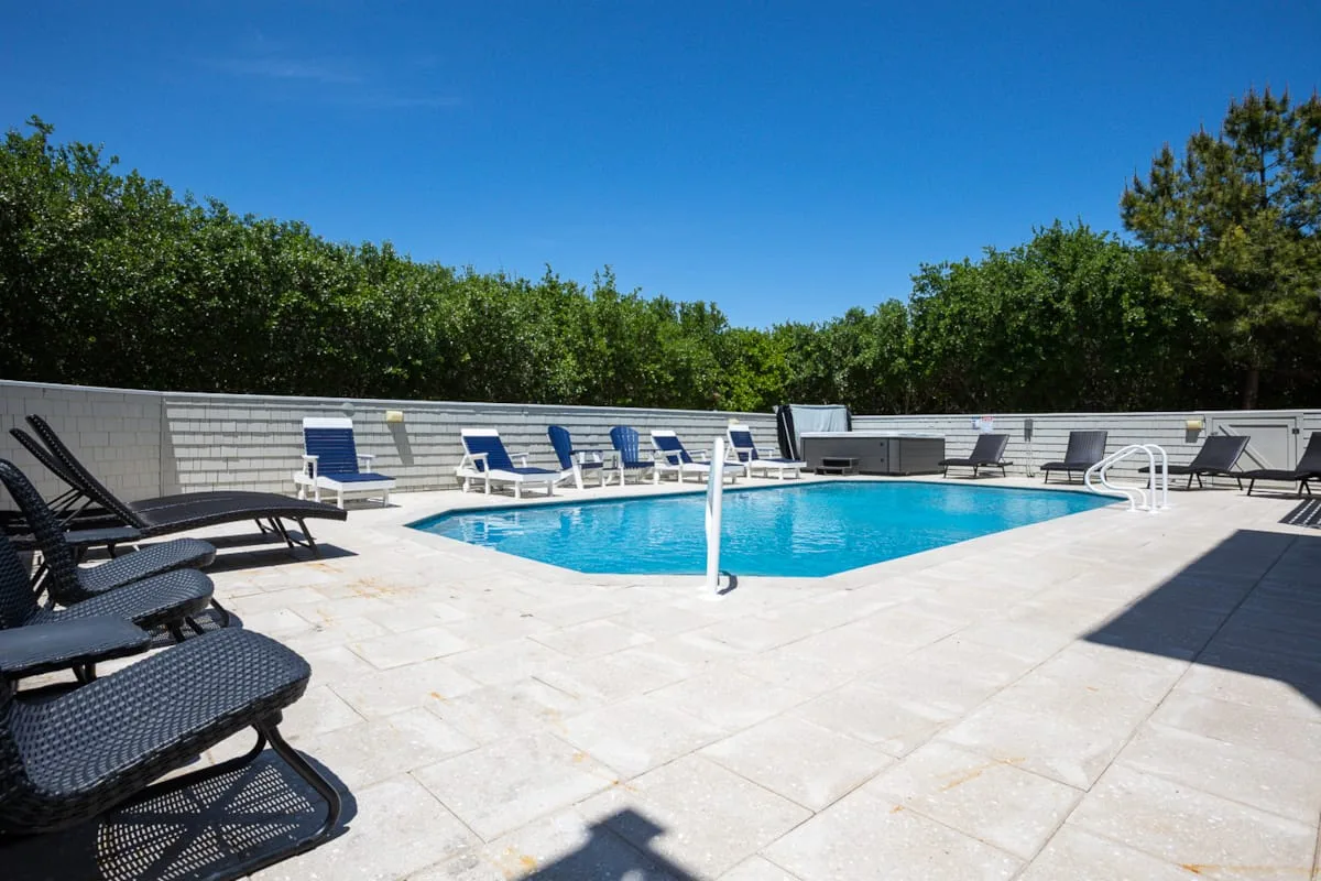 An outdoor swimming pool sits amid a paved deck with lounge seating.