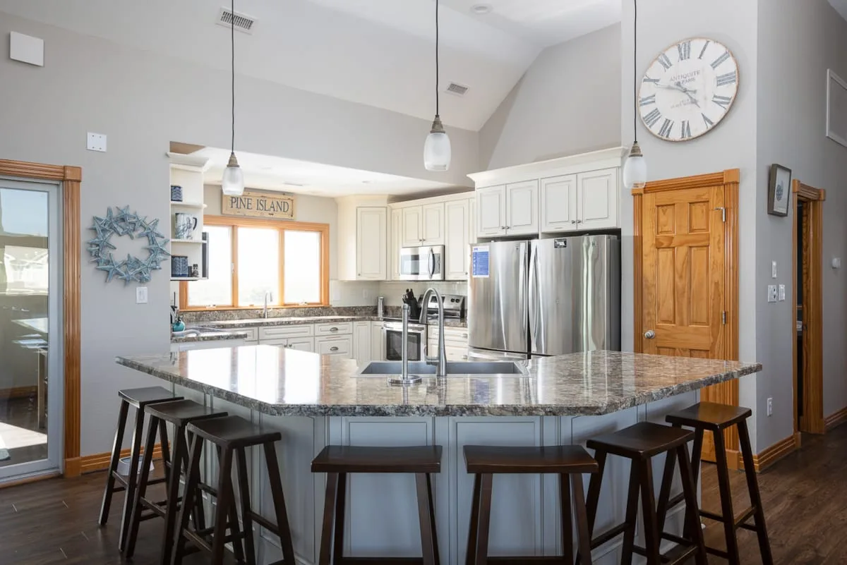 A bright kitchen with a large island, pendant lights, and stainless steel appliances.