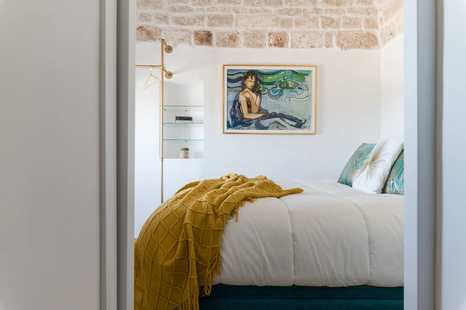 Un dormitorio con una cama bien arreglada y una obra colorida sobre ella.