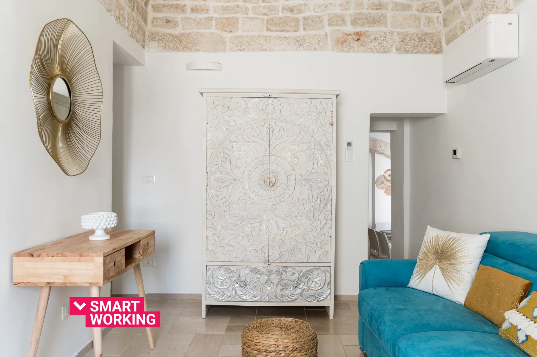 Una sala luminosa con un sofá azul, un escritorio de madera y un armario ornamentado.
