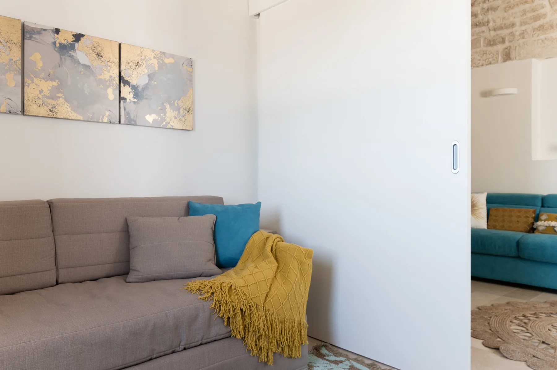 Una sala de estar con un sofá gris, cojines azules y una manta amarilla.