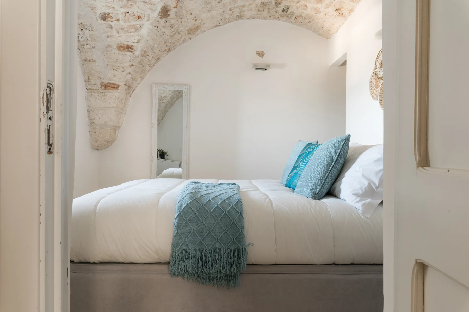 Un dormitorio con ropa de cama blanca y cojines azules bajo un arco de piedra.