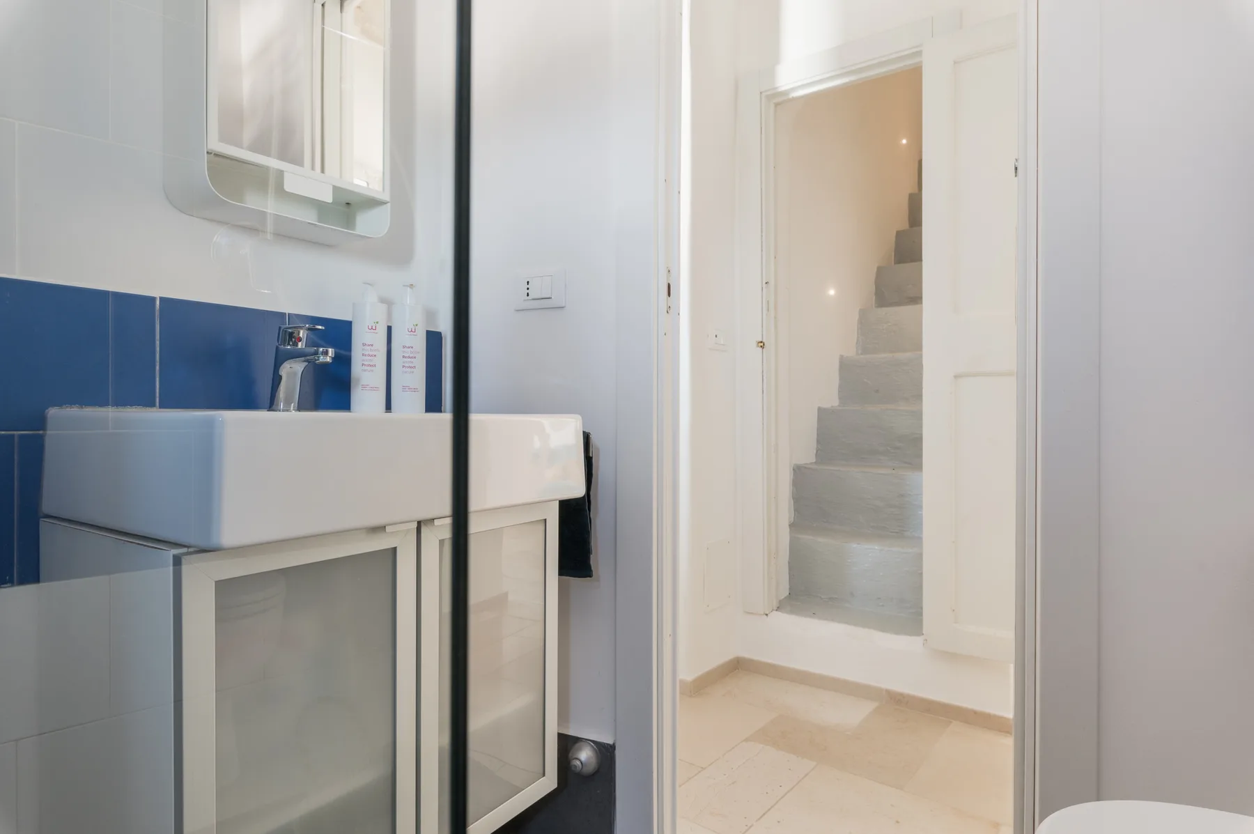 Un baño con lavabo y una puerta abierta hacia una escalera.