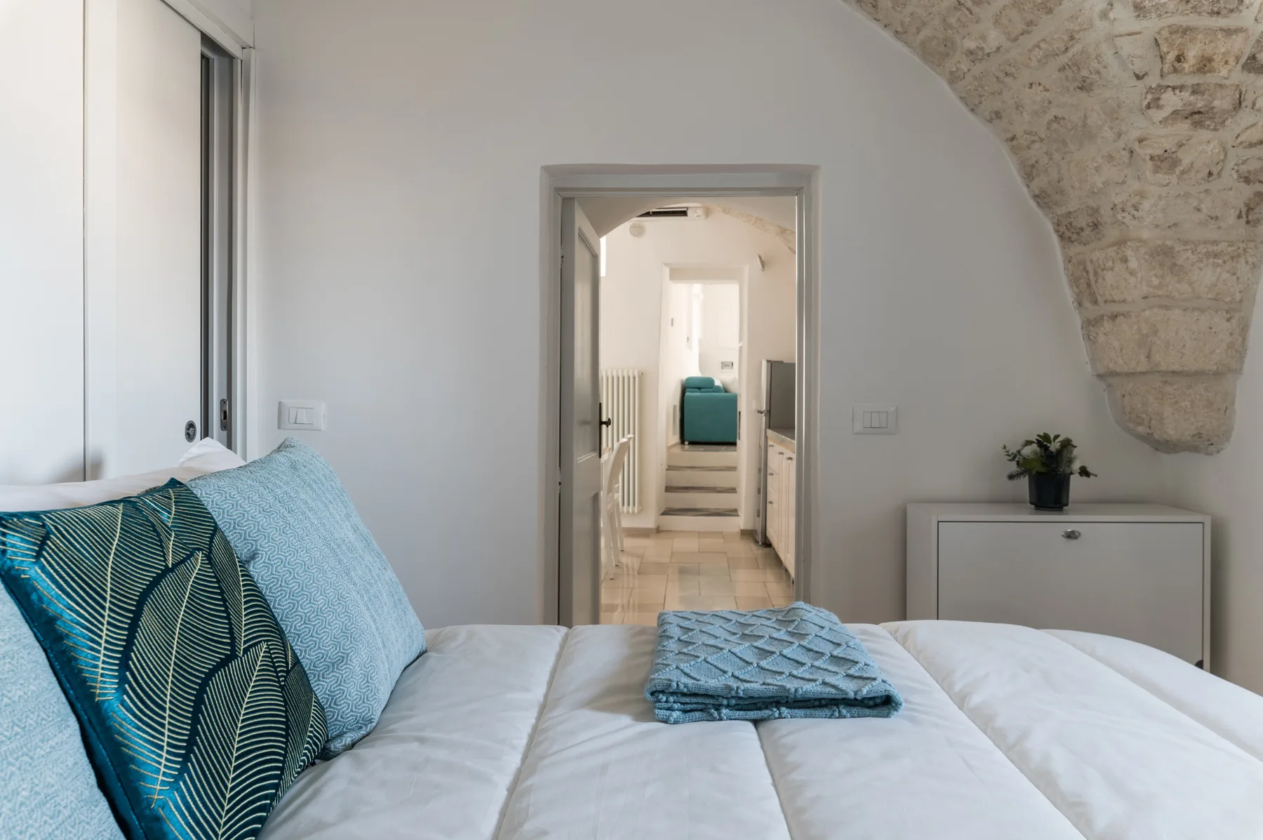 Un dormitorio con una cama y ropa de cama azul doblada bajo un techo de piedra curvo.