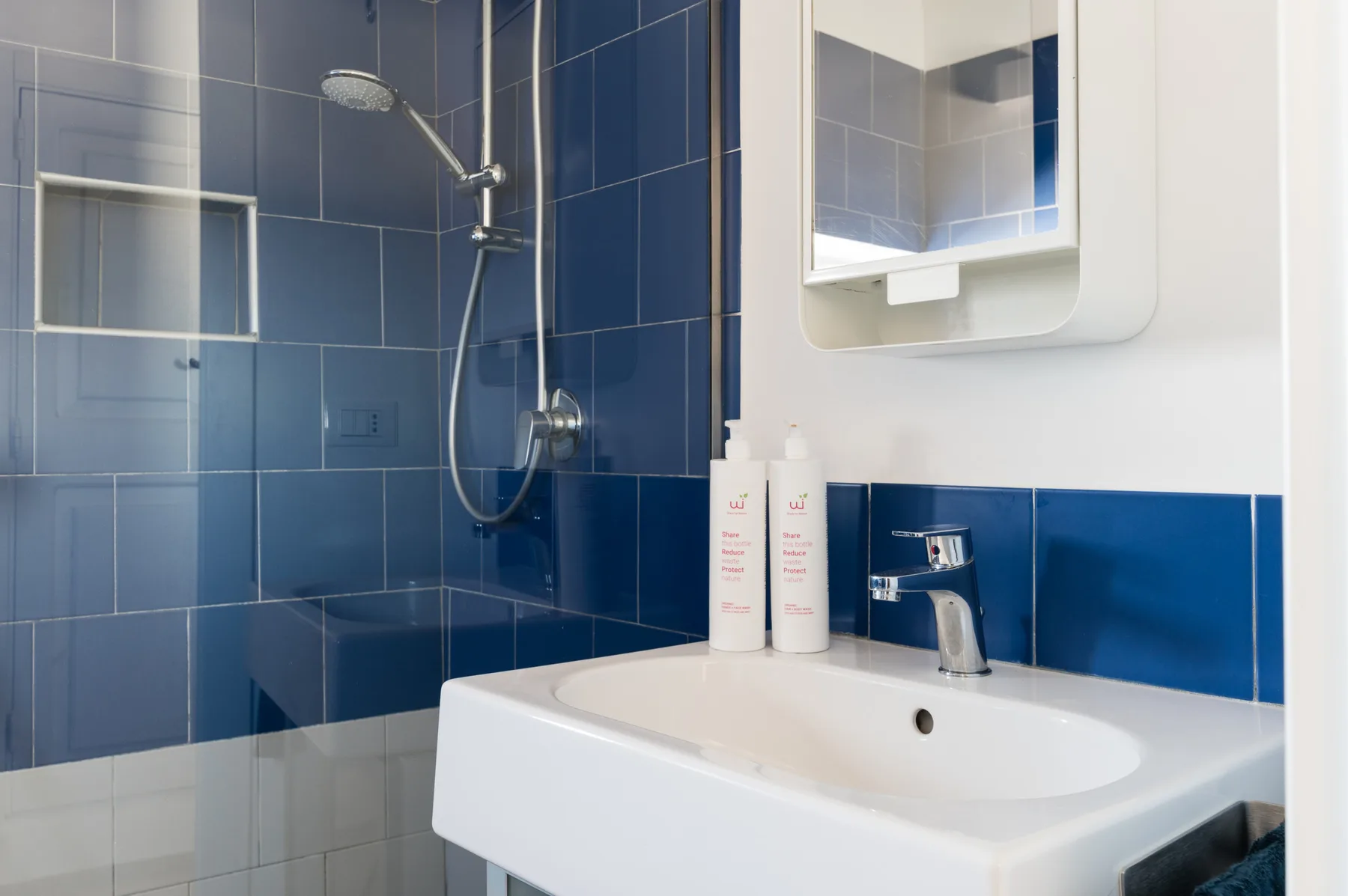 Un baño con azulejos, lavabo, espejo y ducha.