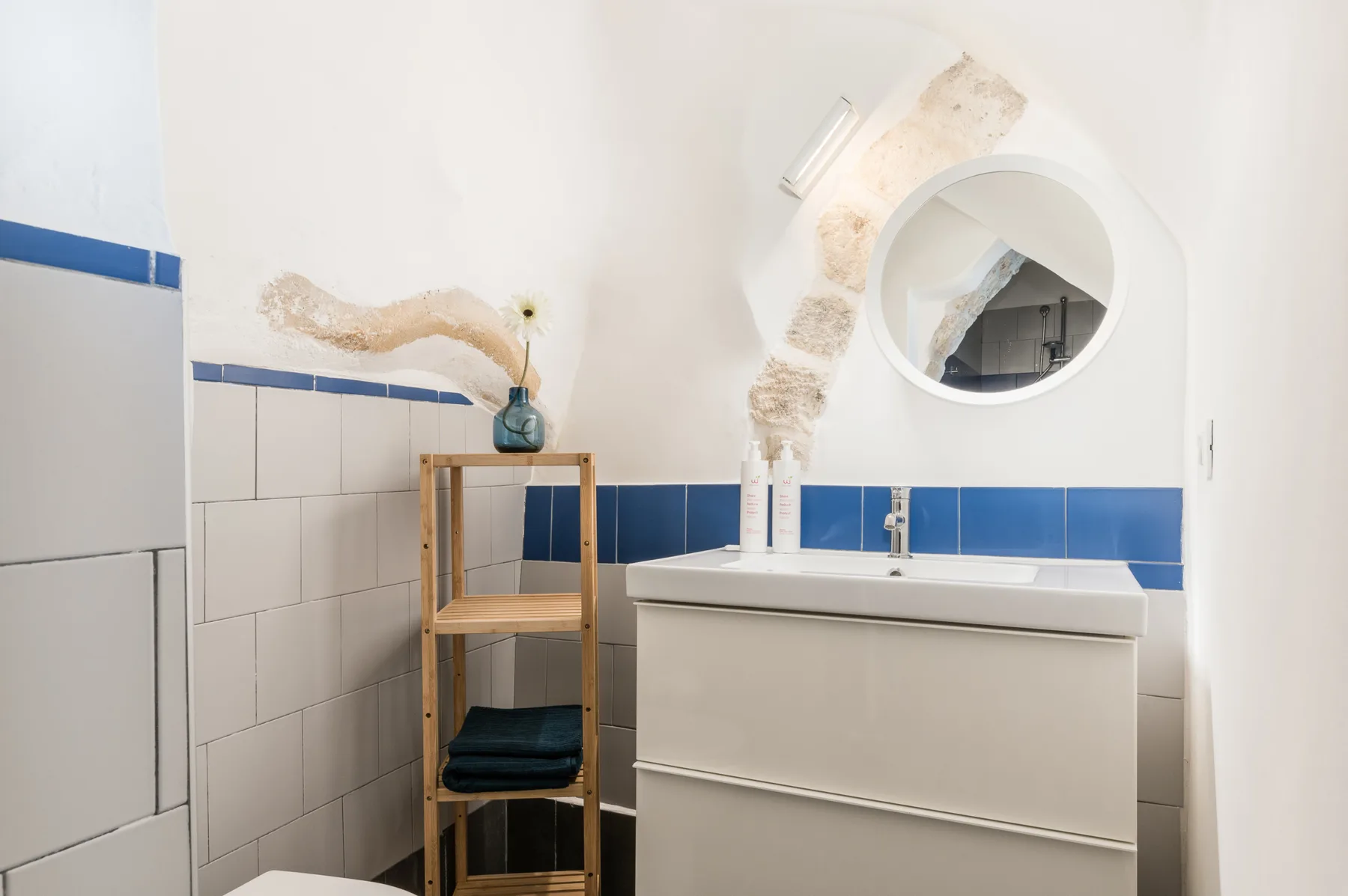 Un baño con un lavabo blanco, azulejos azules y un espejo redondo.