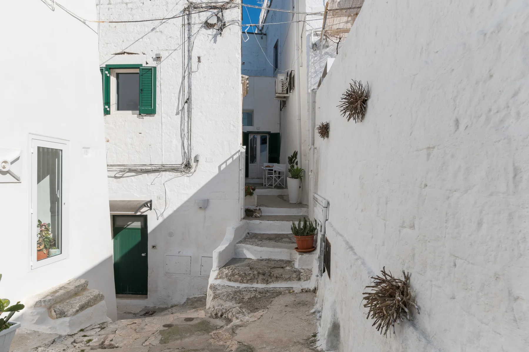 Un callejón estrecho encalado con escalones de piedra y contraventanas verdes.