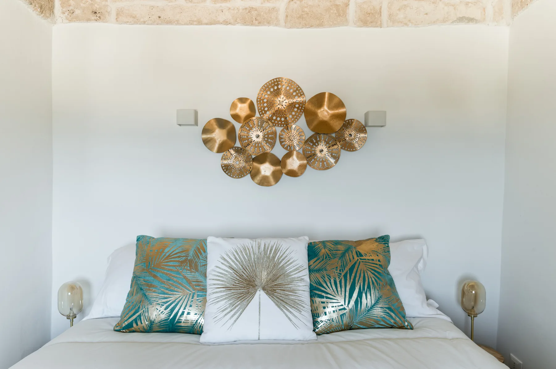 Un dormitorio con una cama y cojines estampados bajo un adorno metálico de pared.