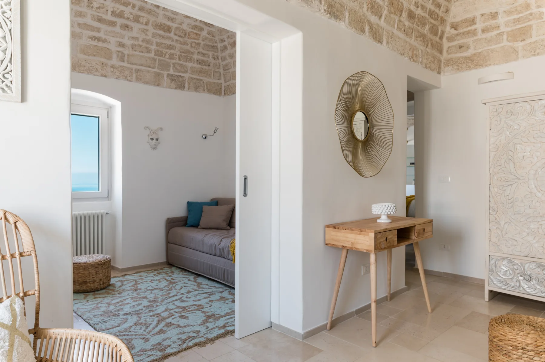 Un dormitorio luminoso con una cama junto a una ventana y una consola de madera en primer plano.
