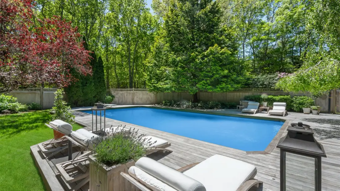 Una piscina en el patio está rodeada por una terraza de madera y árboles frondosos.