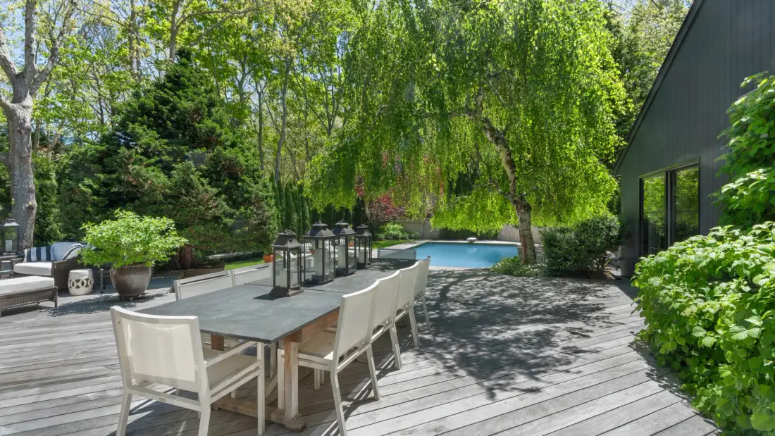 Una zona de comedor exterior a la sombra, con mesa y asientos junto a una piscina.