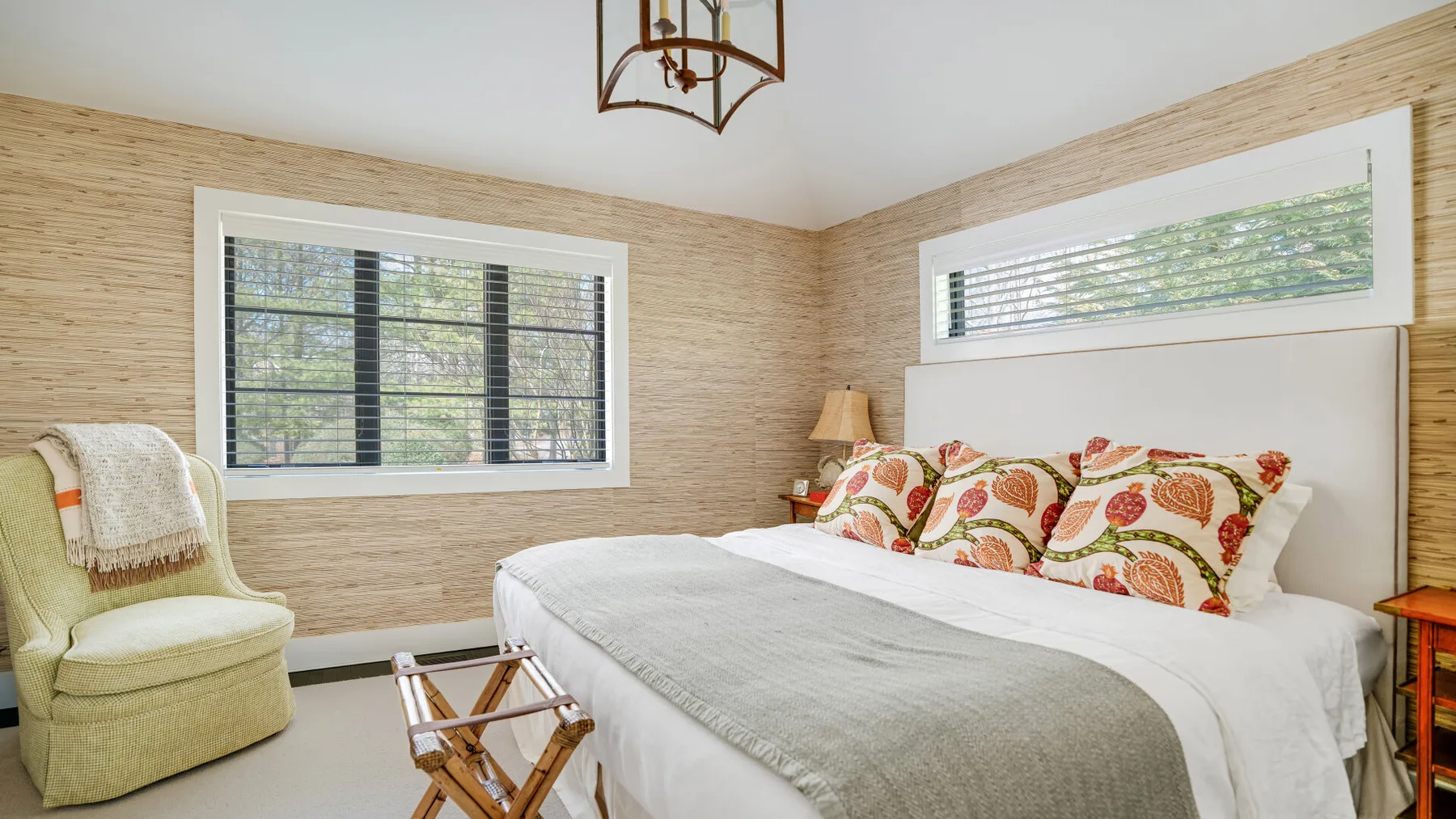 A bedroom with a bed, patterned pillows, and a light-colored armchair.